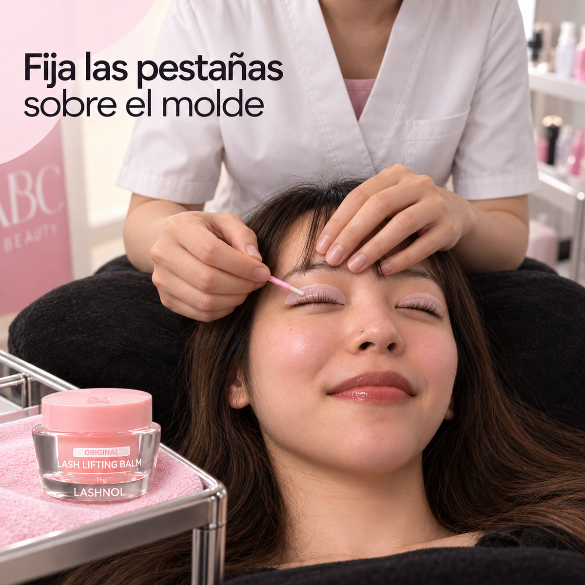 Profesional situada detrás de la cabeza de la modelo acomoda las pestañas sobre el molde; frasco de Bálsamo LASHNOL Original 15 g en primer plano.